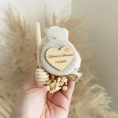 Honigglas des Brautpaares als personalisiertes Gastgeschenk zur Hochzeit, mit Herzanhänger, Holzlöffel und eleganter Dekoration