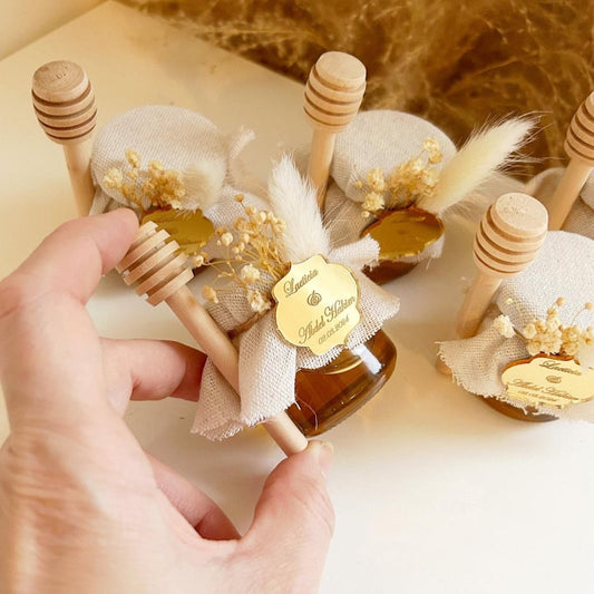 Weißes Prestige-Honigglas als personalisiertes Gastgeschenk für Hochzeit und Taufe, mit Holzlöffel und eleganter Dekoration