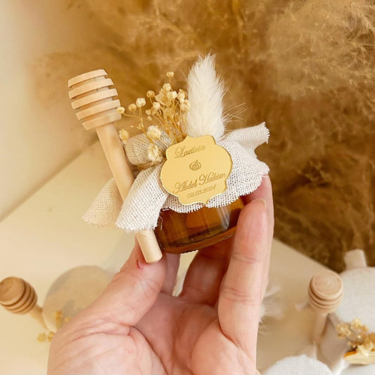 Weißes Prestige-Honigglas als personalisiertes Gastgeschenk für Hochzeit und Taufe, mit Holzlöffel und eleganter Dekoration