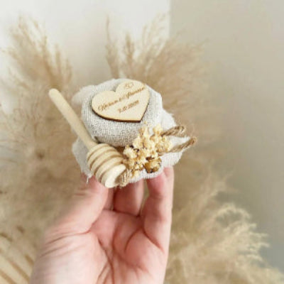 Honigglas des Brautpaares als personalisiertes Gastgeschenk zur Hochzeit, mit Herzanhänger, Holzlöffel und eleganter Dekoration
