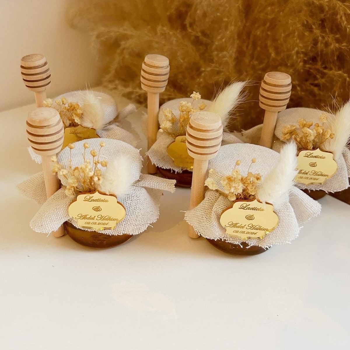 Weißes Prestige-Honigglas als personalisiertes Gastgeschenk für Hochzeit und Taufe, mit Holzlöffel und eleganter Dekoration