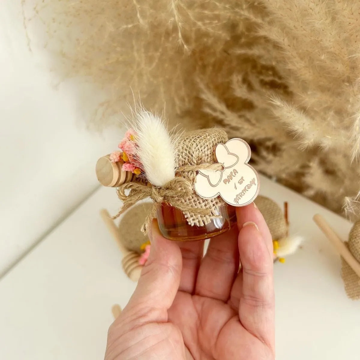 Zauberhaftes Honigglas als personalisiertes Gastgeschenk zur Taufe, zum Geburtstag und zur Kommunion, elegant dekoriert mit Holzlöffel und Blumen